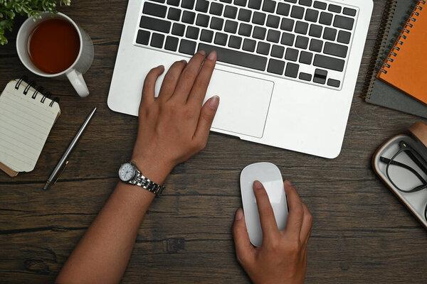 From above with of businesswoman hands holding mouse and typing on laptop computer.