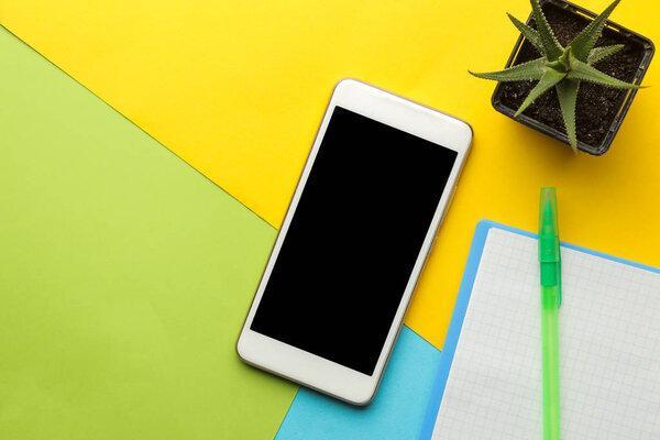 Smartphone. White phone, notepad and flower on a bright multi-colored background. top view. space for text