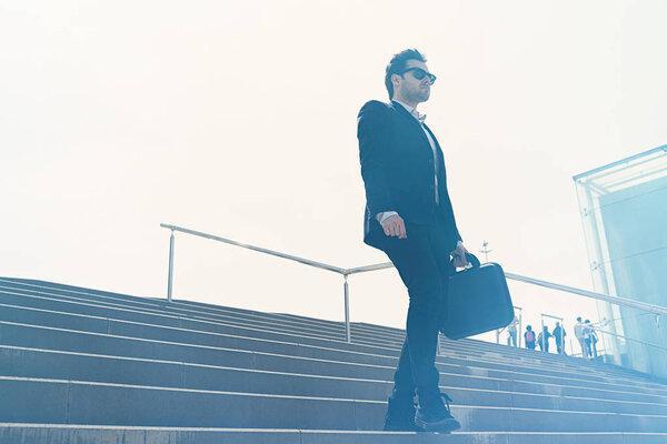 Young confidental businessman wearing suit and running fast downstairs. Horizontal outdoors shot
