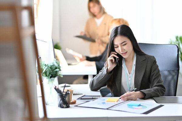 Beautiful asian businesswoman checking financial reports and talking on mobile phone.