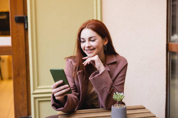 happy woman with red hair using smartphone on summer terrace 