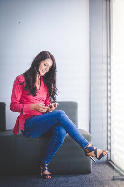 Business woman sitting in her office working and using  her mobile smart phone