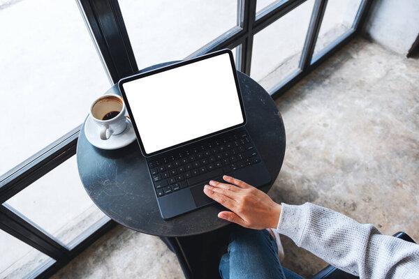 Top view mockup image of a hand using and touching tablet touchpad with blank white desktop screen as computer pc with coffee cup on the table
