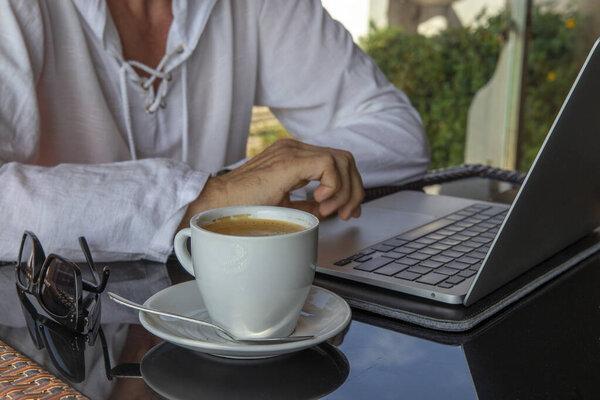 Man freelancer working on laptop, keyboarding text and going to drink coffee at the beach cafe. Working outdoors. Freelance concept