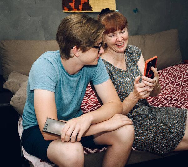 Home photo teenage son talking to phone with mom while sitting on sofa