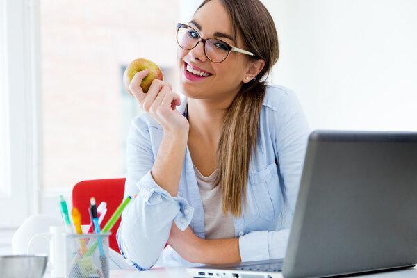Pretty young woman eating an apple in her office.