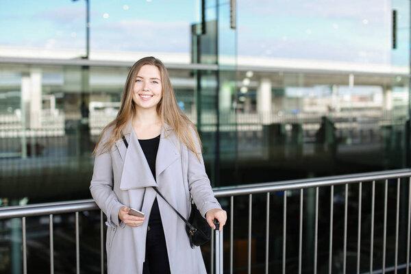 Woman standing with valise and smartpone near airport.