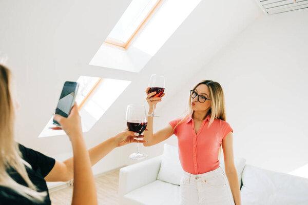 Friends heaving fun, drinking whine and making photos on smartphone, celebrating success or spending their leisure time.