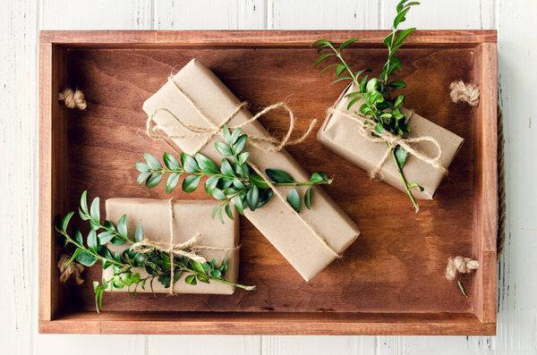 Modern Christmas wrapped presents with natural decor on white wooden background. Gifts boxes in craft paper with twine and green branches. Seasonal greetings card. Top view. Flat lay.