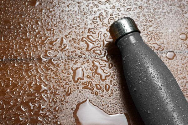 Stainless steel thermos bottle isolated on a wooden table sprayed with water. Black color