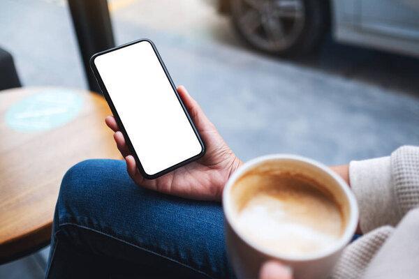 Mockup image of a woman holding mobile phone with blank white desktop screen while drinking coffee 