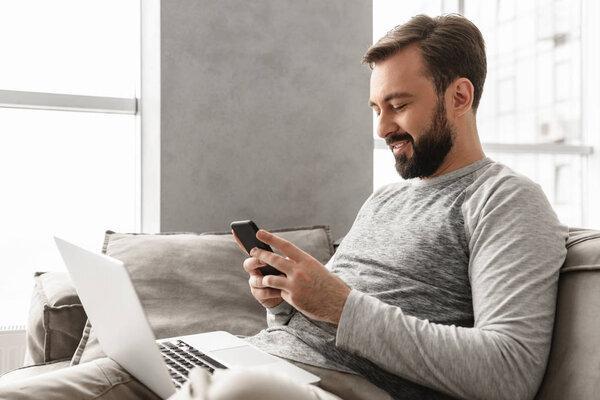 Image of caucasian man 30s in casual wear sitting on sofa in liv