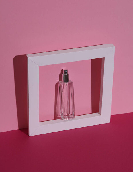 Perfume bottle in white frame on a pink background with shadow. Beauty concept. Creative layout, minimalism
