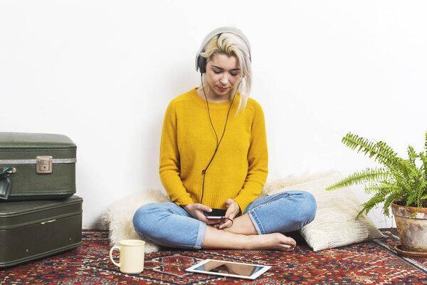 Happy young blonde woman sitting on floor with headphones and tablet