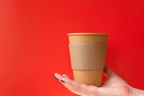 Kraft paper coffee cup in hand on the red background