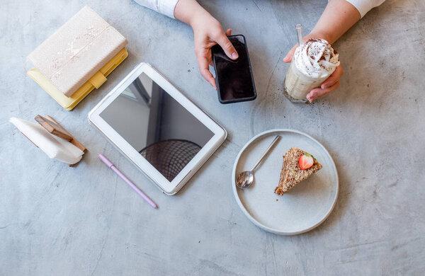 Young woman in a cafe works on a smartphone while sitting in a cafe. Blond business woman in white clothes. New normal concept. Flat lay