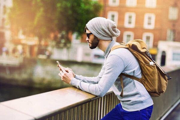 City, travel and man with phone on balcony for network, communication and search of location. Internet, male person and backpack with technology for outdoor commute, information and tourism in London.