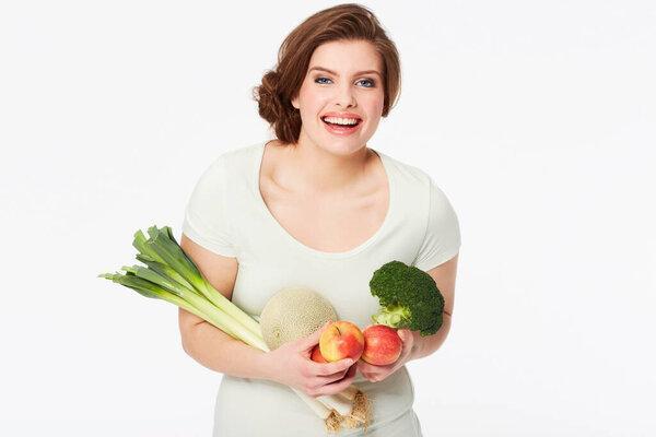 Woman, happy and portrait with vegetables in studio, nutrition and wellness for vegan diet in mock up. Person, smile face and fruit for food, vitamins and detox in nutritionist by white background.