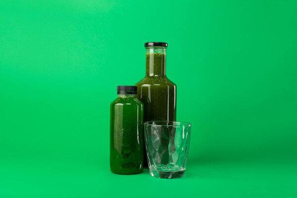 Fresh celery spinach juice in a plastic and glass bottle and an empty glass nearby, isolated on a green background. Healthy diet detox juice