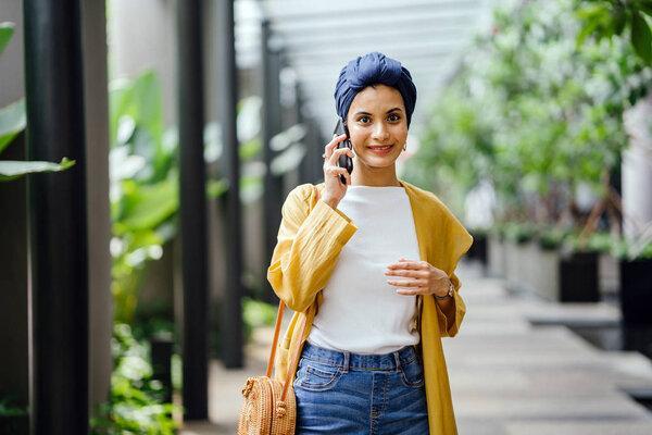 Young and attractive Malay Muslim woman walking down steps and talking on her smartphone during the day