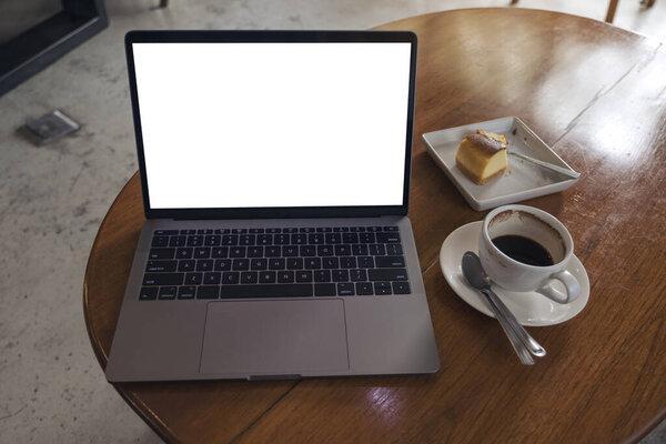 Mockup image of laptop with blank white desktop screen with coffee cup and cake on wooden table in modern cafe