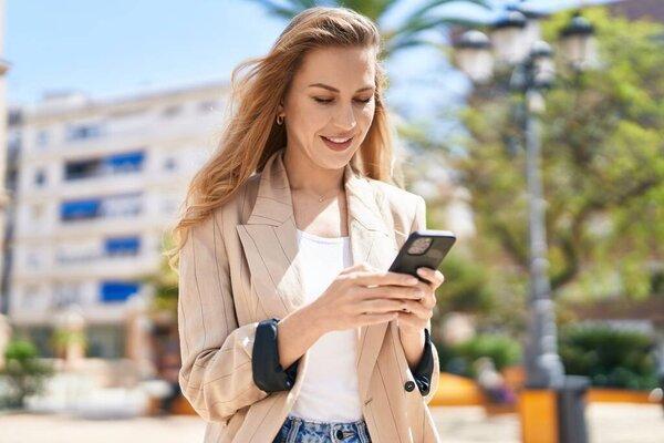 Young blonde woman smiling confident using smartphone at park