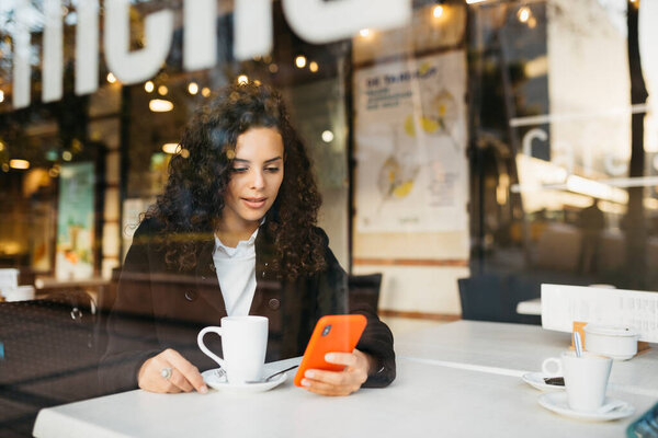 Young woman using a red smartphone  and drinking coffee in a coffeeshop