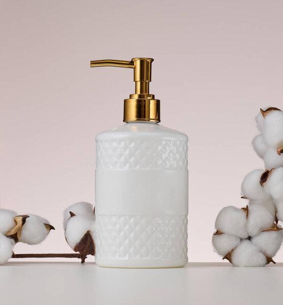 White plastic container with a golden dispenser on a beige background. Container for liquid soap, shampoo