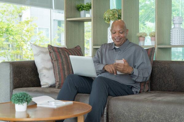 Business senior old elderly Black American man, African person using a smartphone or mobile phone in living room at home in technology device concept. Lifestyle people.
