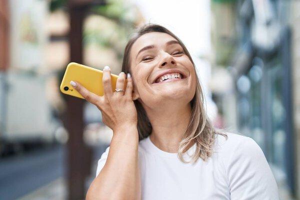 Young caucasian woman smiling confident listening audio message by the smartphone at street