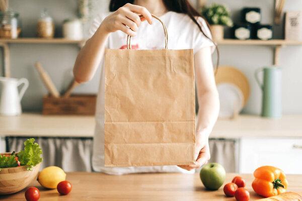 Caucasian woman hold eco shopping bag with fresh vegetables on the table in modern kitchen.
