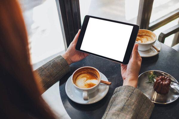 Mockup image of a woman sitting and holding black tablet pc with blank white desktop screen in cafe