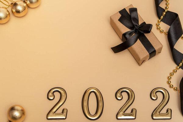 New Year 2022. Top view New Year mockup on beige background: black ribbon, gift box, golden numbers and multicolored sparkles. Layout of postcards, invitations.