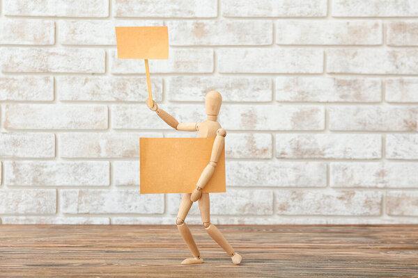 Wooden mannequin with blank placards near brick wall