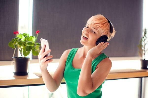 Young woman with short hair listening for music with headphones indoor. People and lifestyle concept