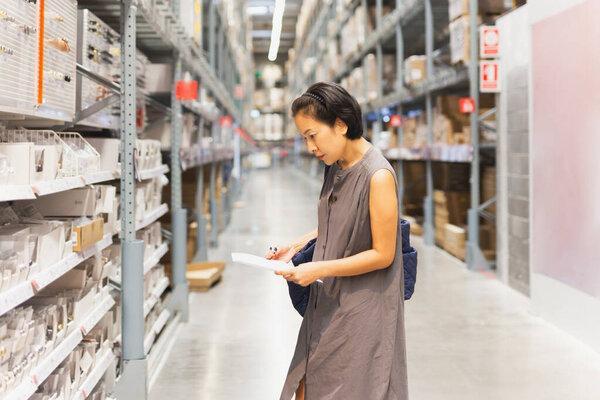 妇女持有在仓库中选择家庭用品的文件