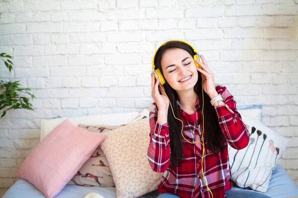 Beautiful young woman listening to music in headphones at home