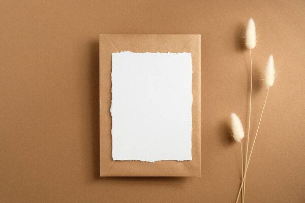 Wedding invite and envelope mockup on brown background with dried flowers. Flat lay, top view.