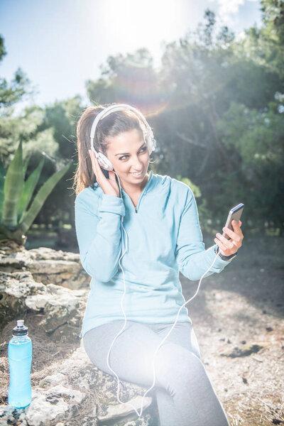 Young female runner is having break and listening to music during the run 
