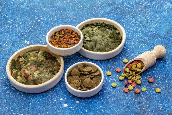 Assorted different types of food for aquarium fish. Flakes, spirulina, pills, mixture. Navy blue sea background