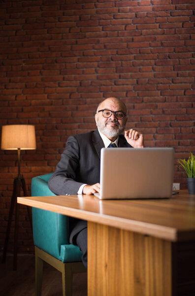 Asian Indian senior financial businessman sitting at his workstation or desk in front of a computer, laptop and tablet. Speaking on phone while doing some paperwork
