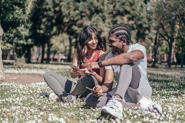 Two interracial friend runners checking mobile phone after jogging outdoors.