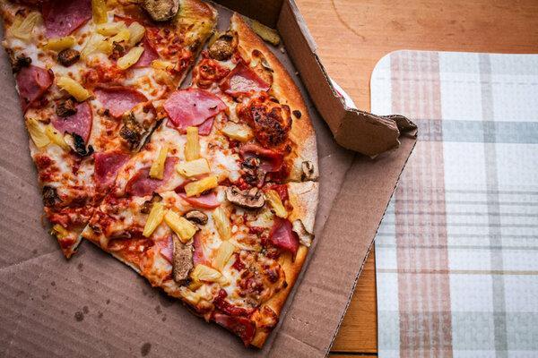 Three slices of pizza that were eaten were left in a cardboard box. Placed on a maple-colored wooden table. And a green plaid placemat.