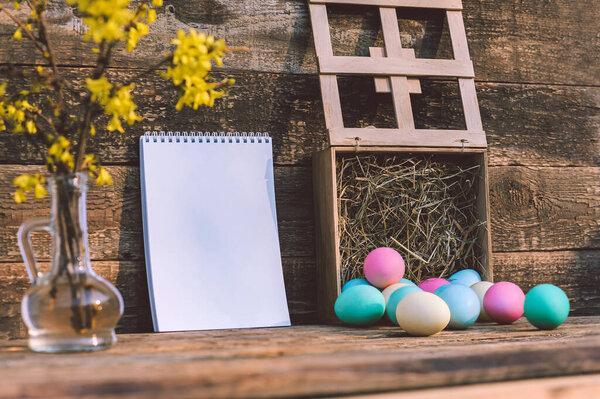 A bunch of colored eggs with hay and a notebook on. Against the background of an old board. Concept on the theme of Easter day