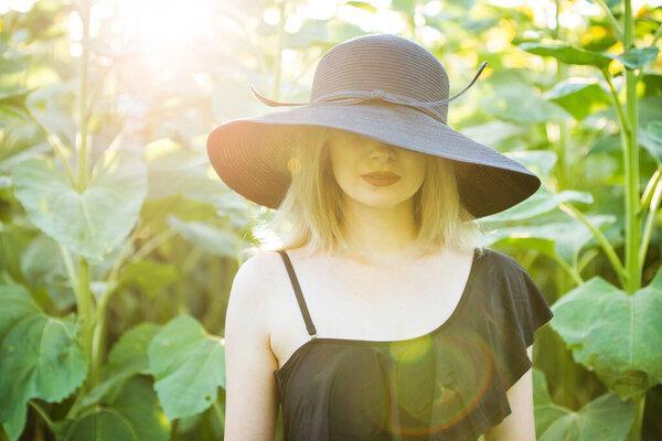 blond european girl in a black swimsuit and hat on nature with sunflowers