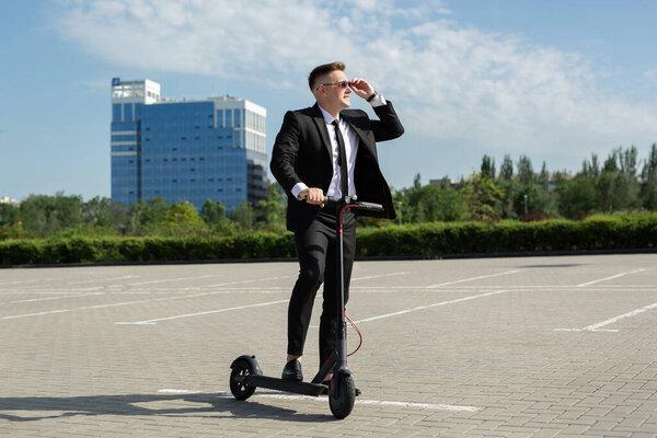 Young businessman with electric scooter standing in front of modern business building looking at watch.