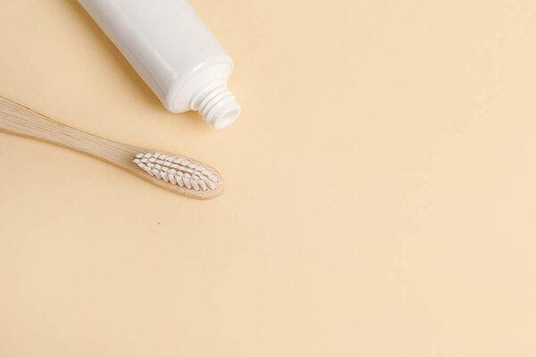 Blank white tube of toothpaste and wood brush on beige background, copy space