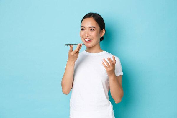 Lifestyle, technology and people concept. Beautiful enthusiastic asian girl record voice message, using smartphone speaker while having conversation, record own voice in mobile app