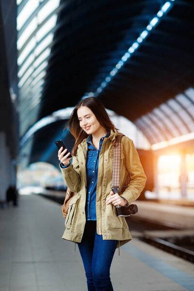 Beautiful young woman using smart-phone while standing on the railway station platform.