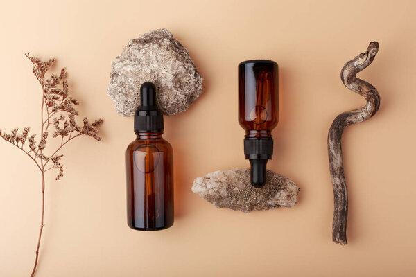 Top view of skin serums in dark bottles against beige background with stones and dry flowers